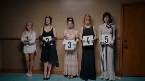 Gif from HBO's Big Little Lies where the five main women characters are standing in ridiculous costumes while holding up numbers during a police lineup.