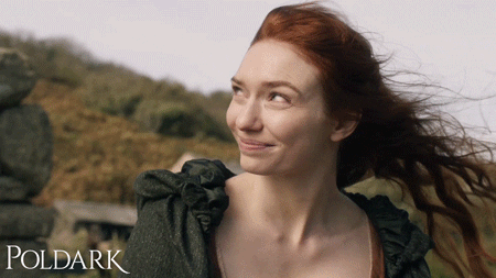 Demelza from Poldark with her red hair blowing in the wind and winking with a sneaky smile.